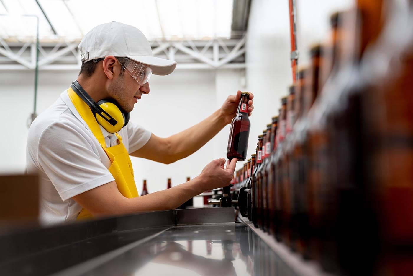 Worker inspecting beer bottles on production line for non-alcoholic brewing and beverage product development