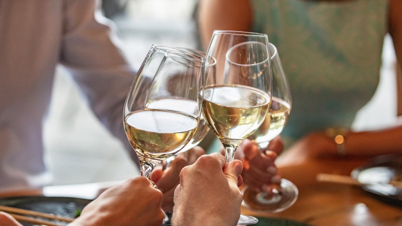 Four people toast with stemmed glasses filled with white wine.